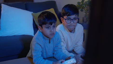 Two-Young-Boys-At-Home-Playing-With-Computer-Games-Console-On-TV-Holding-Controllers-Late-At-Night-1